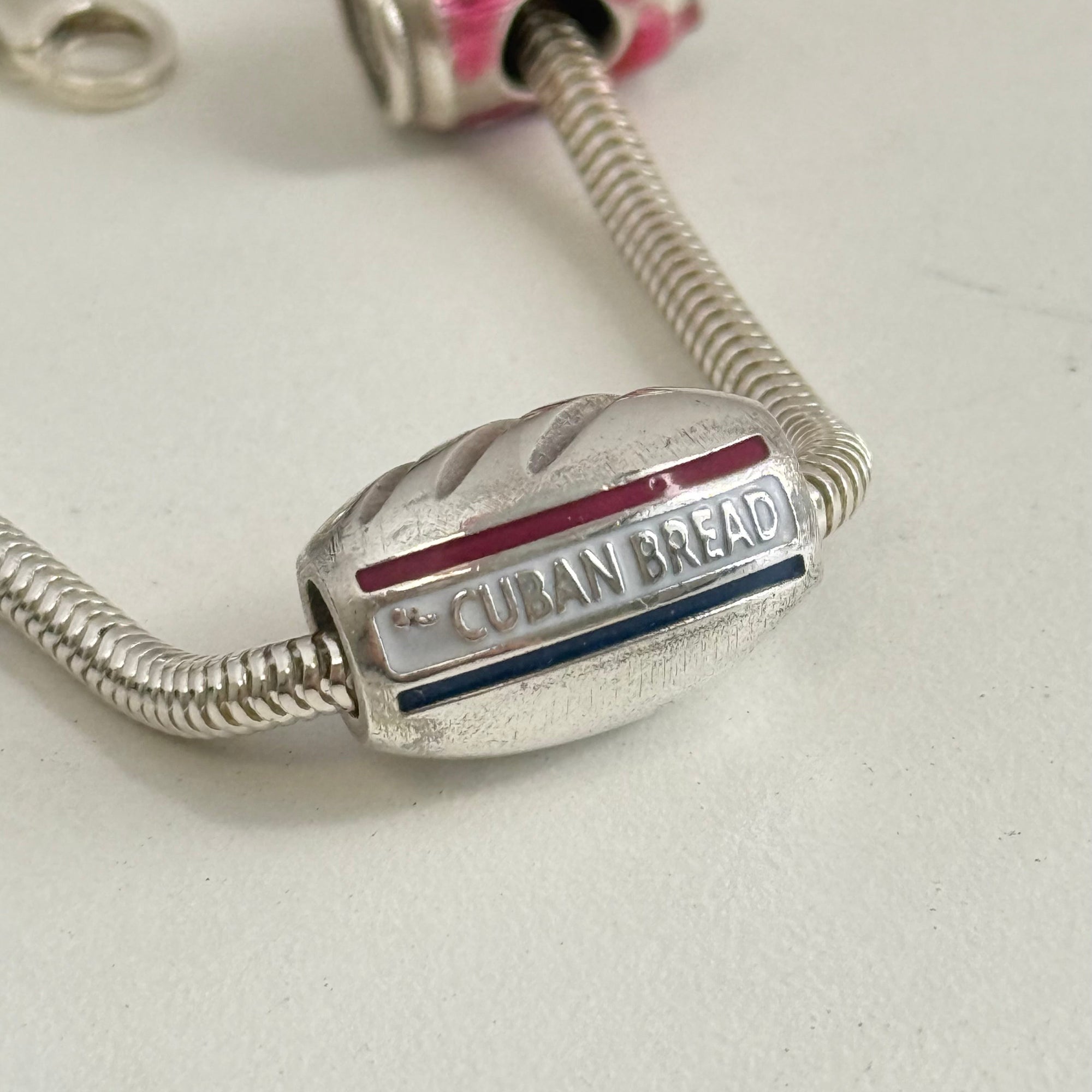Silver charm shaped like a loaf of Cuban bread on a light background