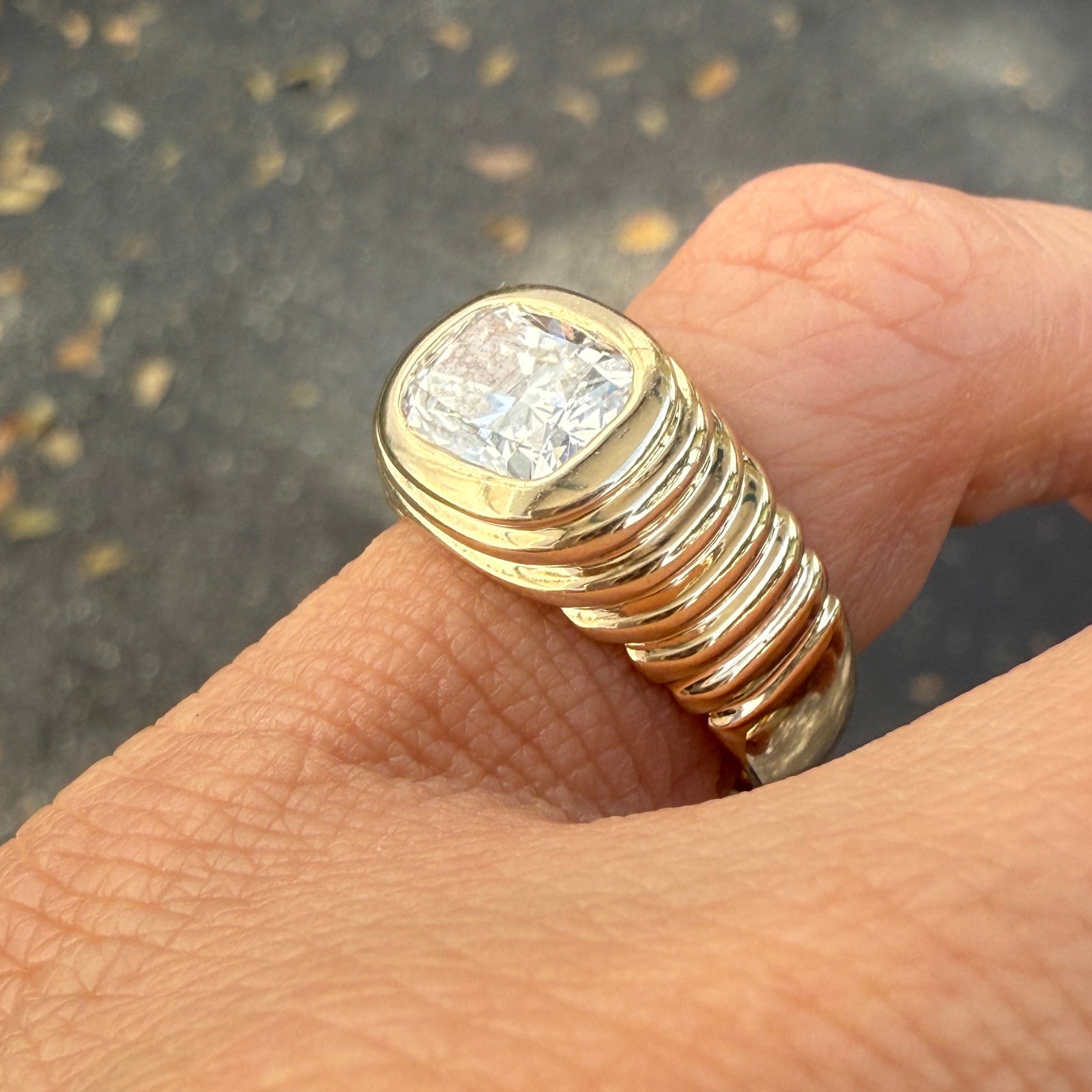 A hand wearing a 14K yellow gold pinky ring with a striped texture and a large center lab diamond.