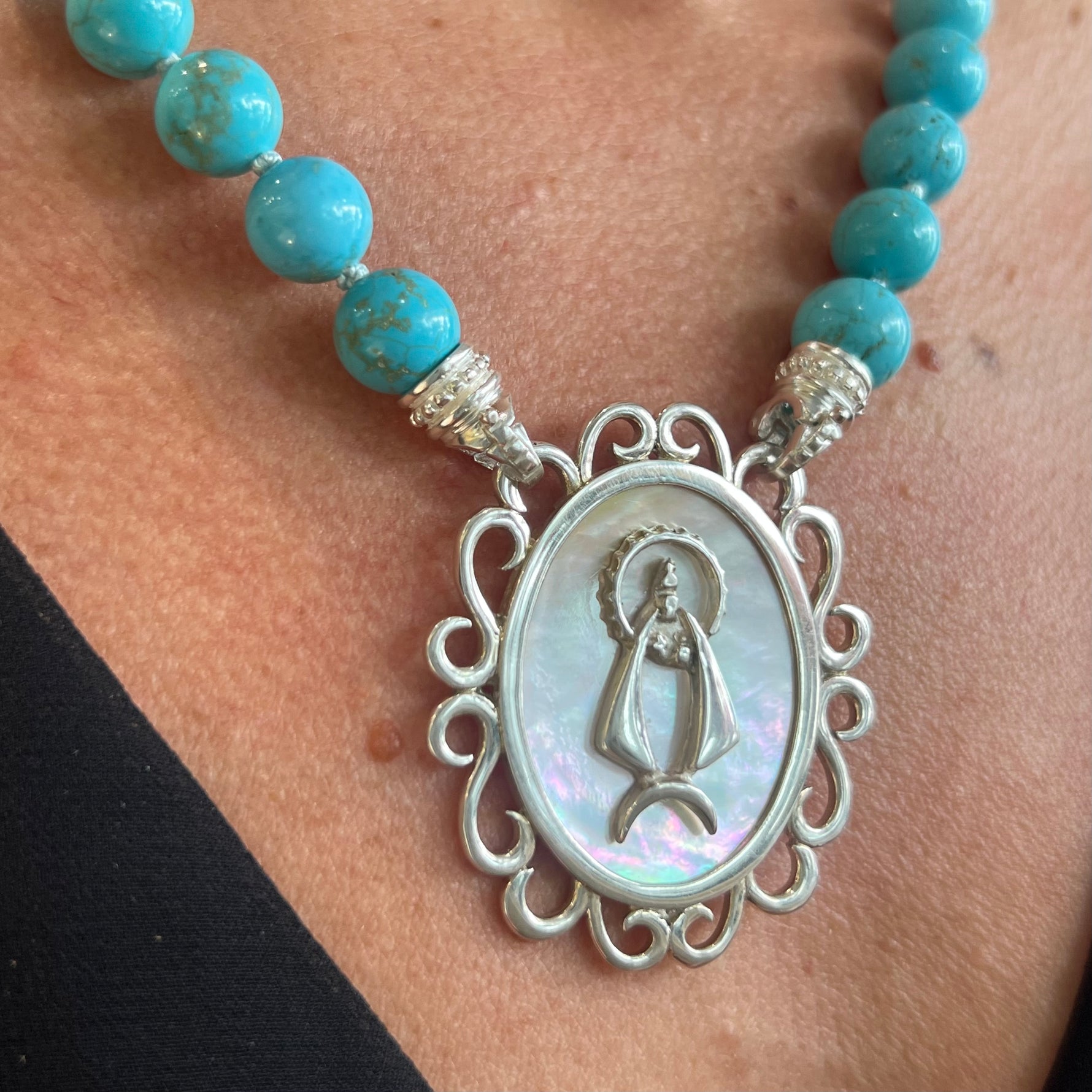 A sterling silver pendant with a mother of pearl center featuring an image of Caridad del Cobre, mounted on a necklace Santayana signature interchangeable necklace. 