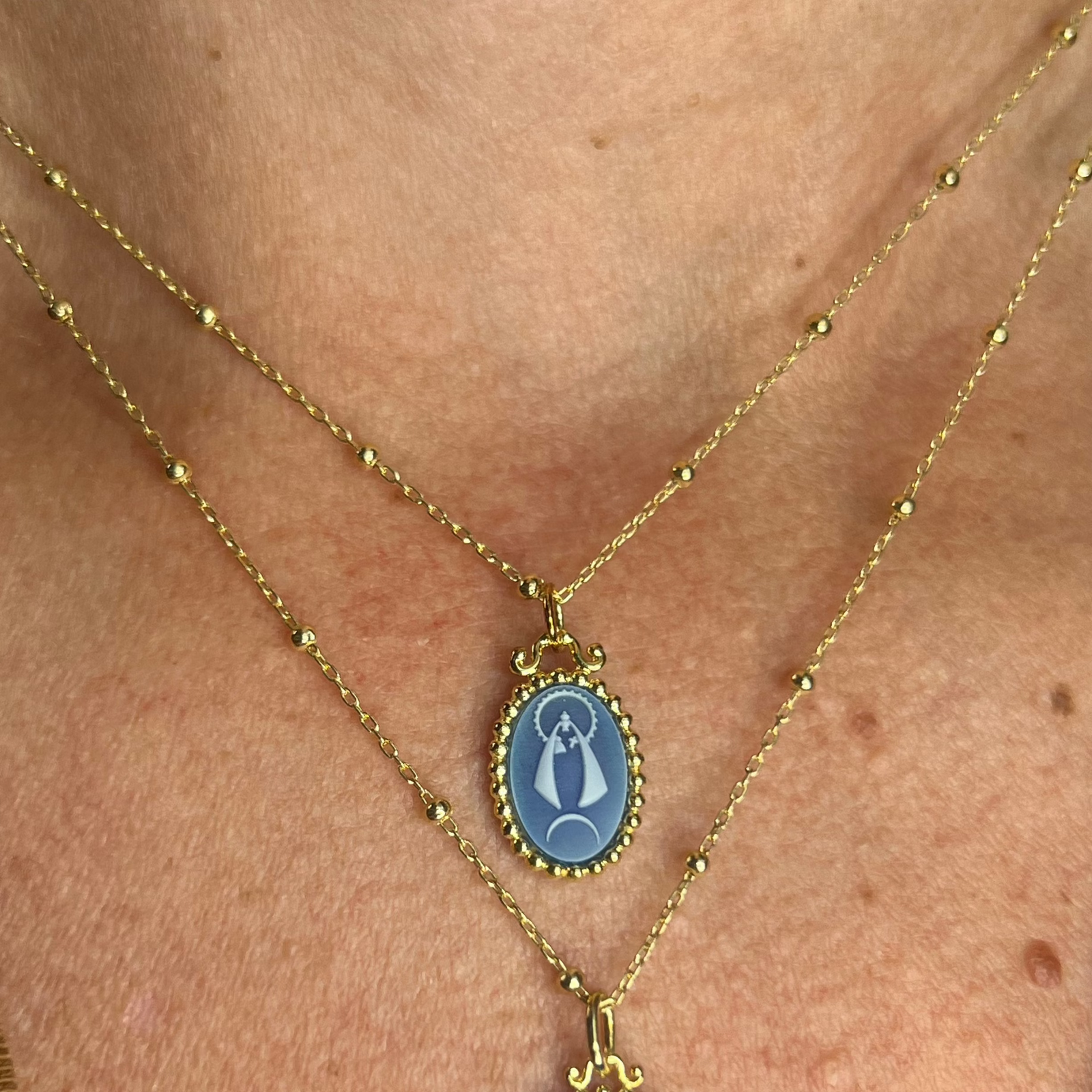 A sterling silver with gold plating Caridad del Cobre pendant necklace featuring a blue agate image of the patron saint of Cuba, on a gold-plated chain.