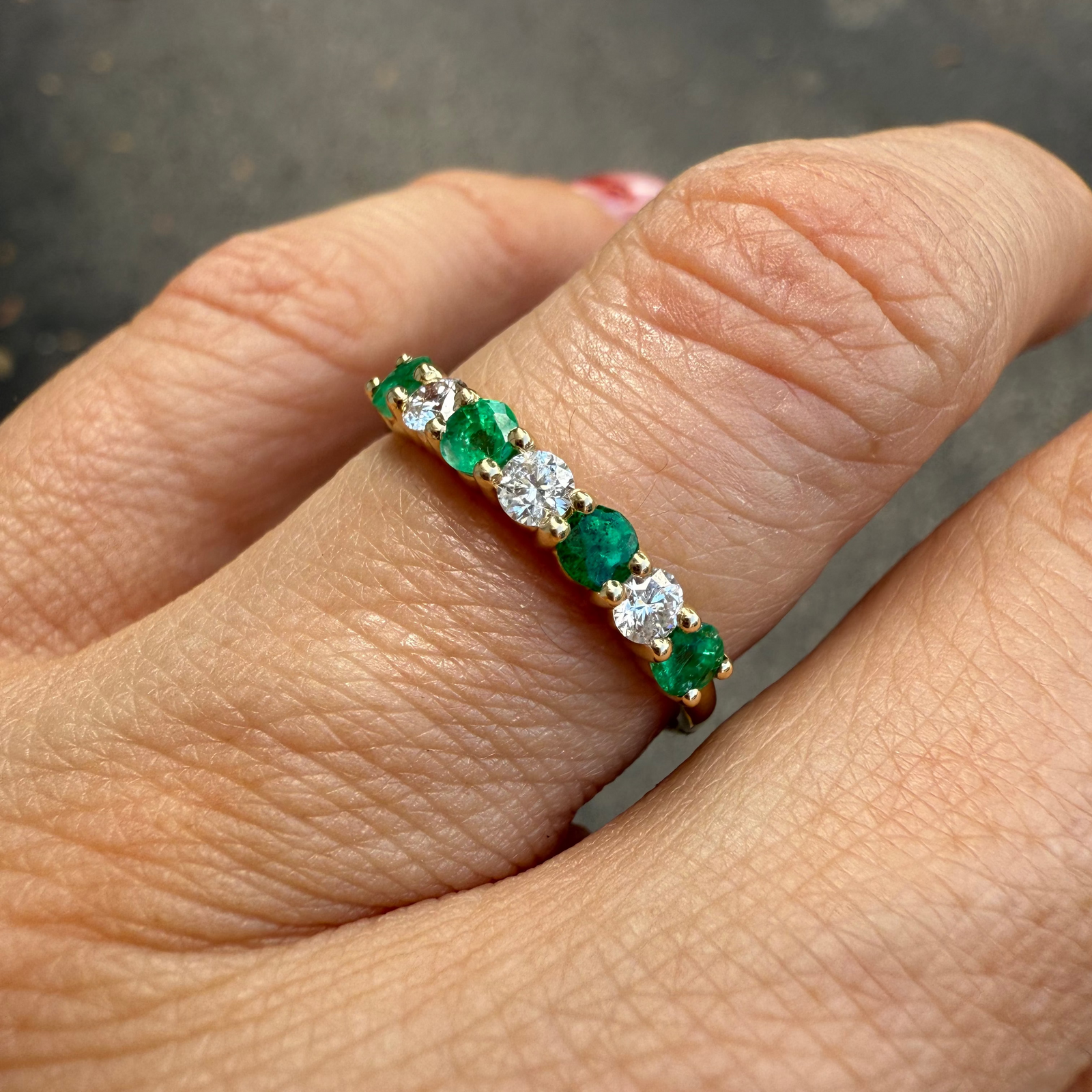 Emerald and diamond band ring in 14K yellow gold held by a hand.