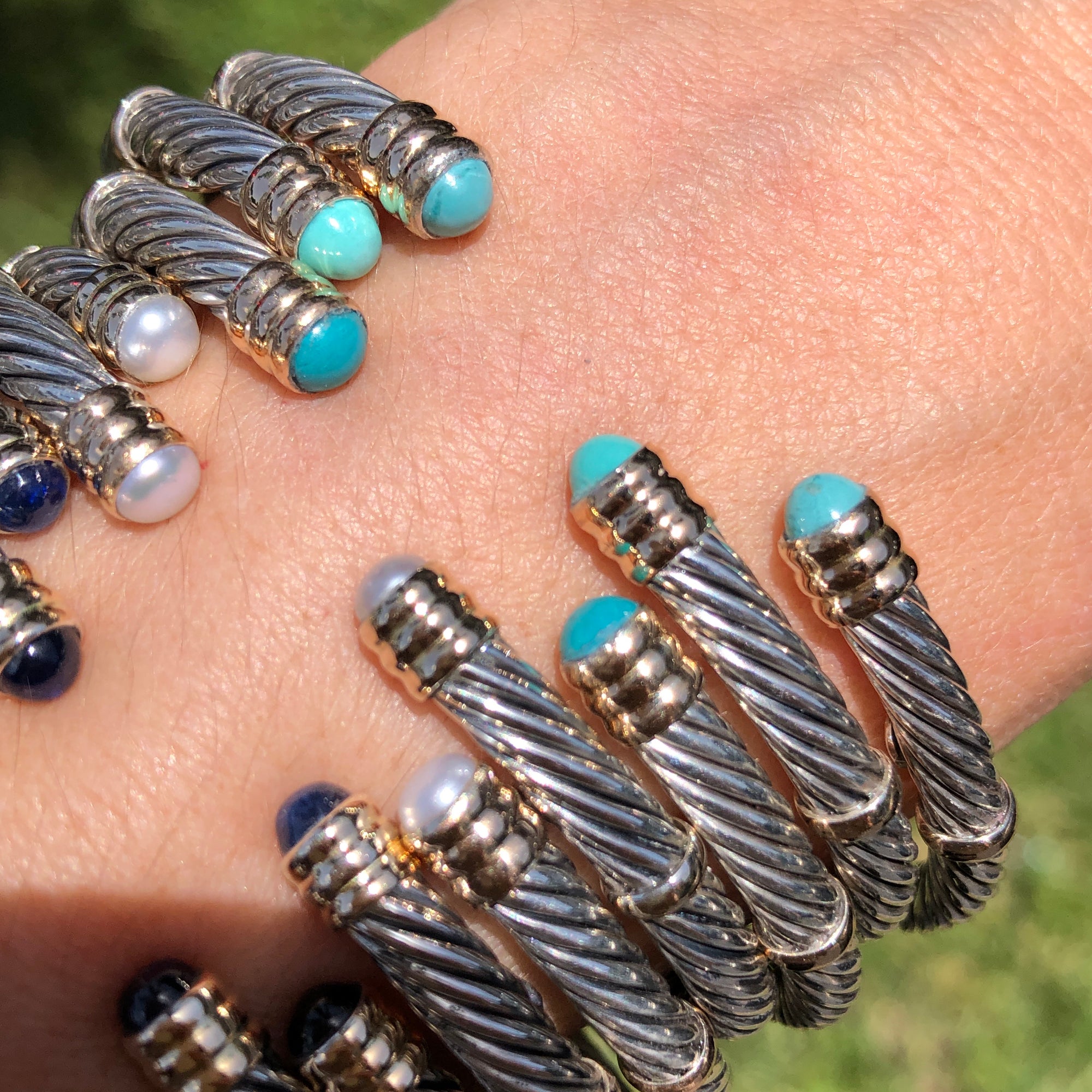 A collection of sterling silver and 14K twist bangles with various stones and pearls displayed on a person&#39;s wrist.