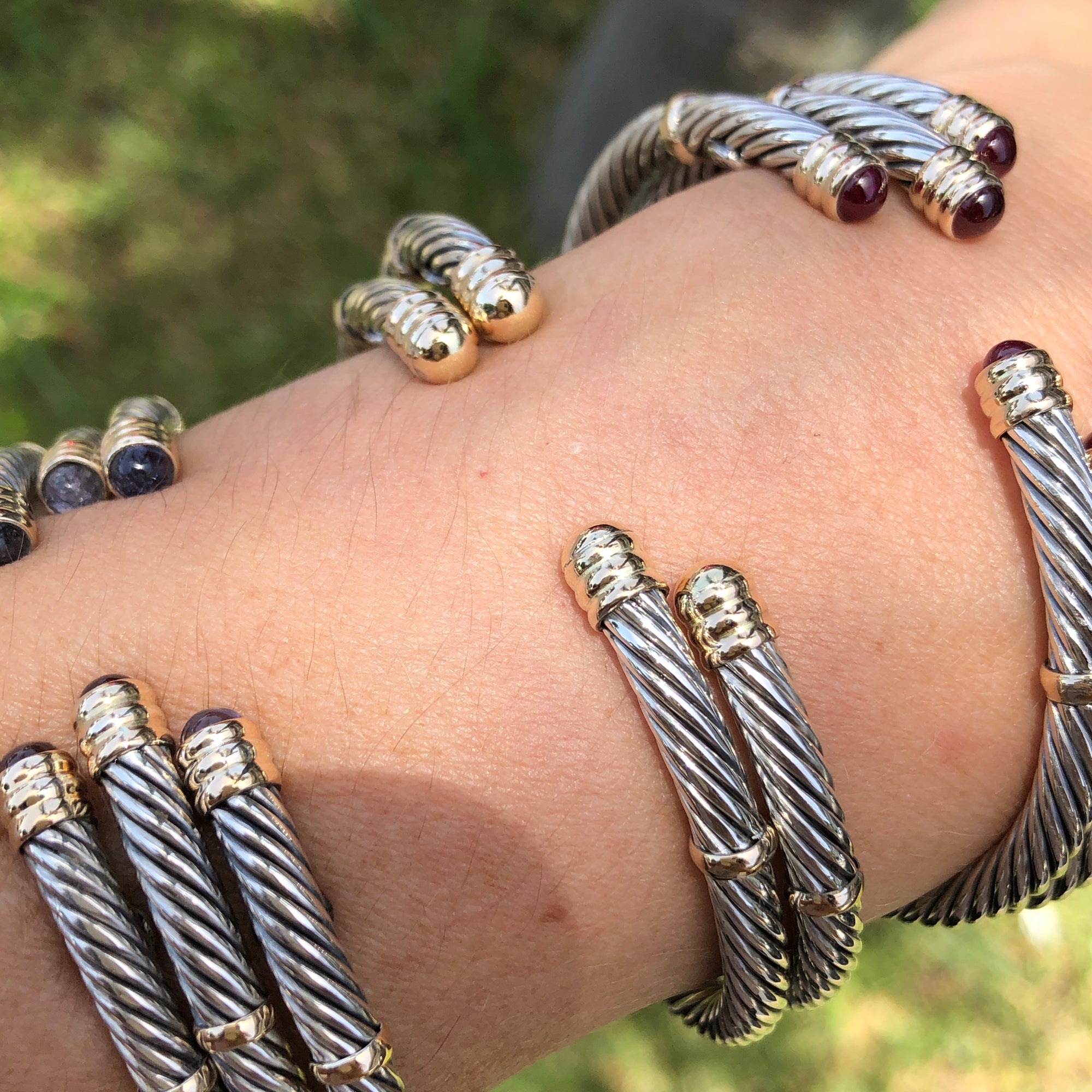A collection of sterling silver and 14K twist bangles with various stones and pearls displayed on a person&#39;s wrist.