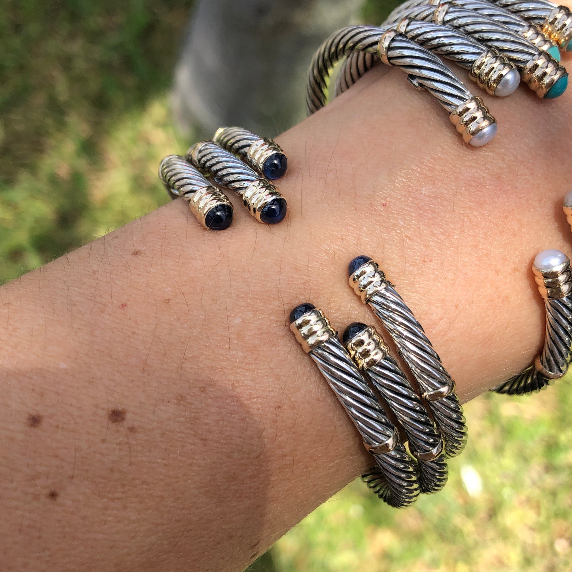 A collection of sterling silver and 14K twist bangles with various stones and pearls displayed on a person&#39;s wrist.