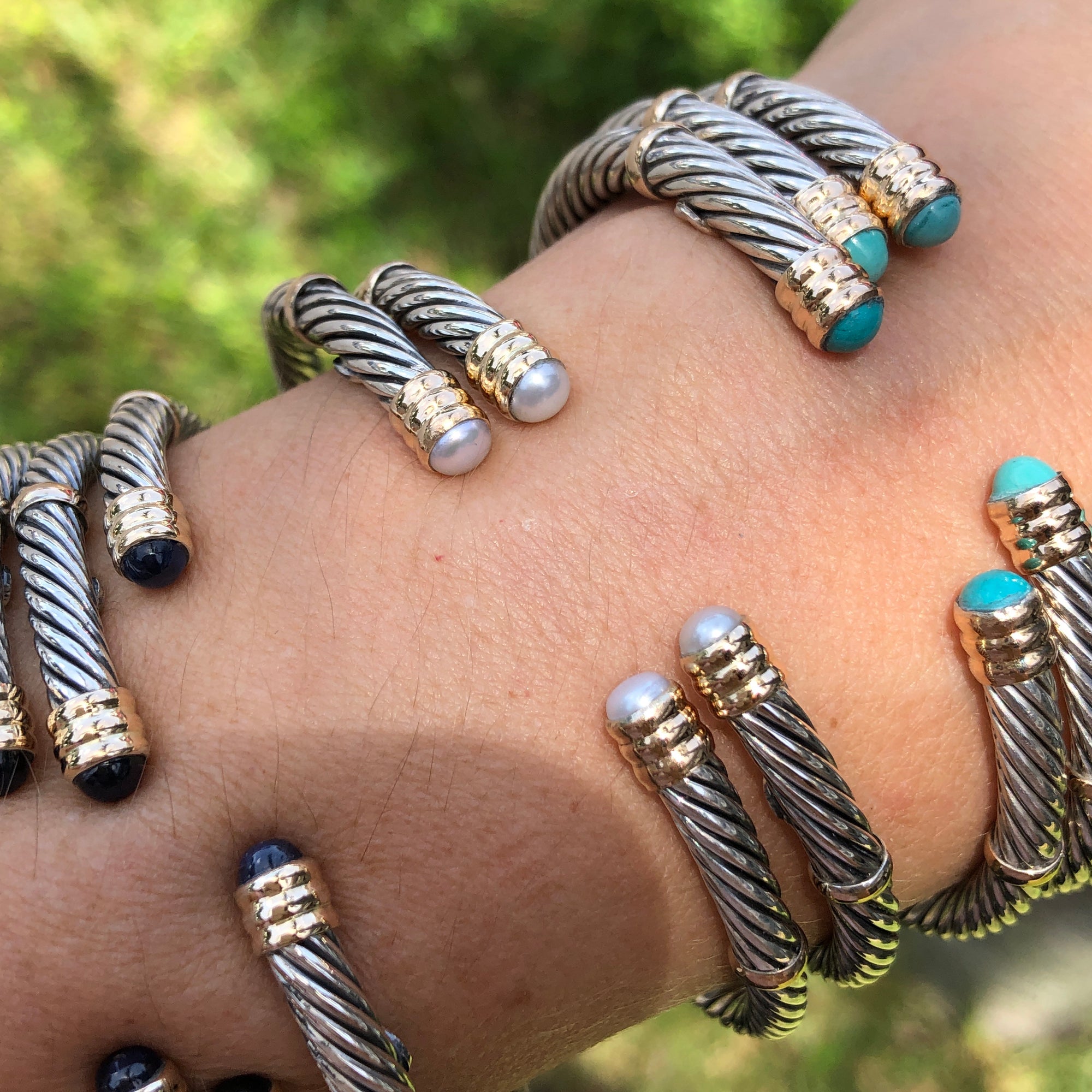 A collection of sterling silver and 14K twist bangles with various stones and pearls displayed on a person&#39;s wrist.